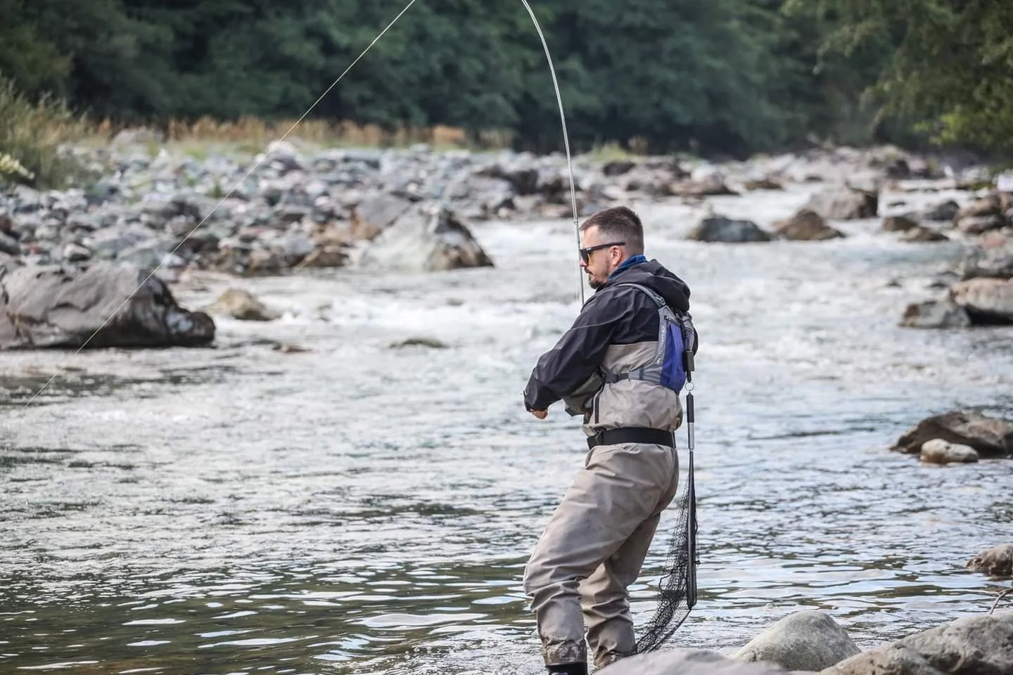 An angler in waders playing a fish with a bent rod on a fast boulder stretch of the Tara.