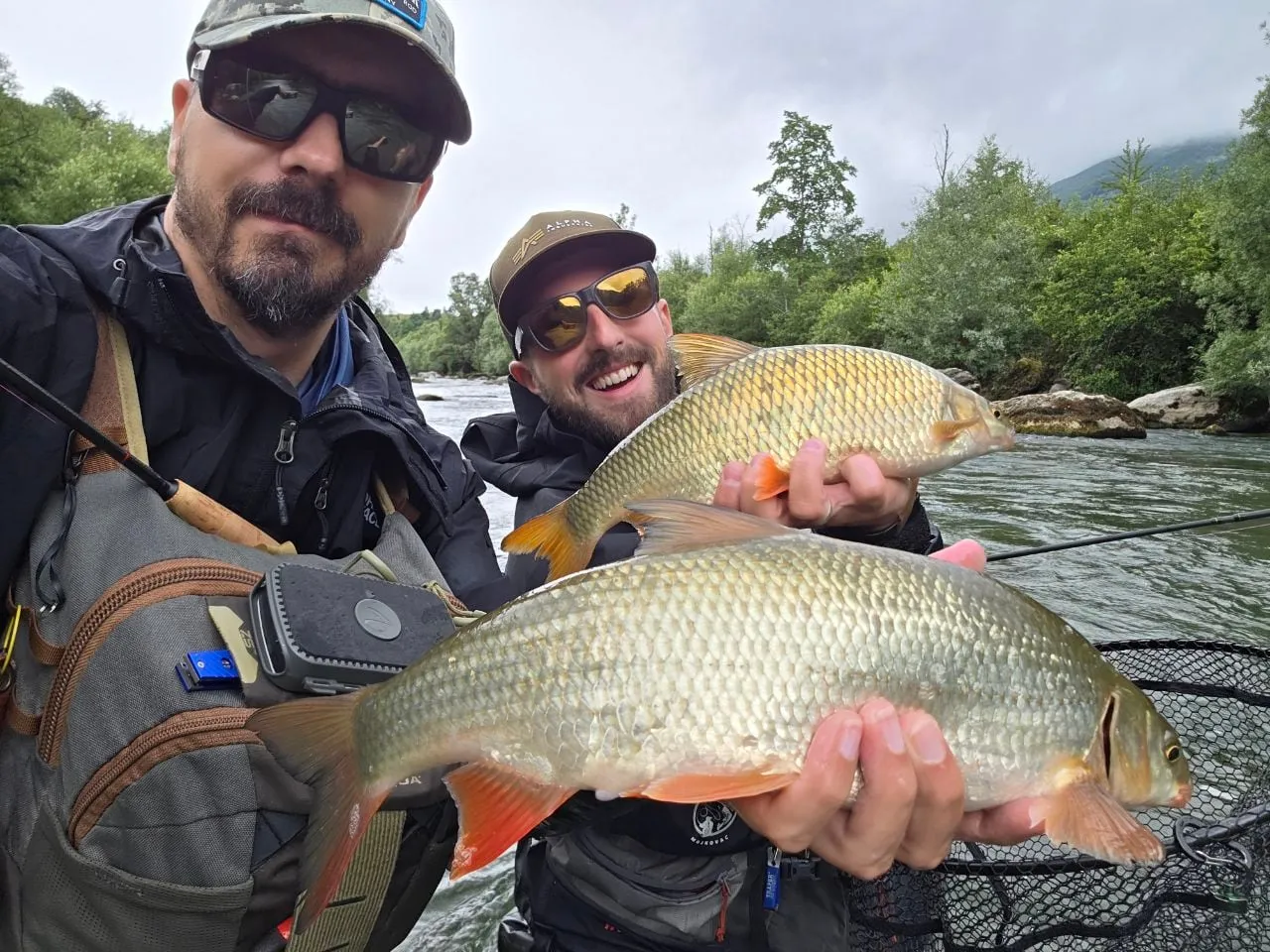 Two anglers on the Lim each holding a large nase, the river and wooded banks behind.