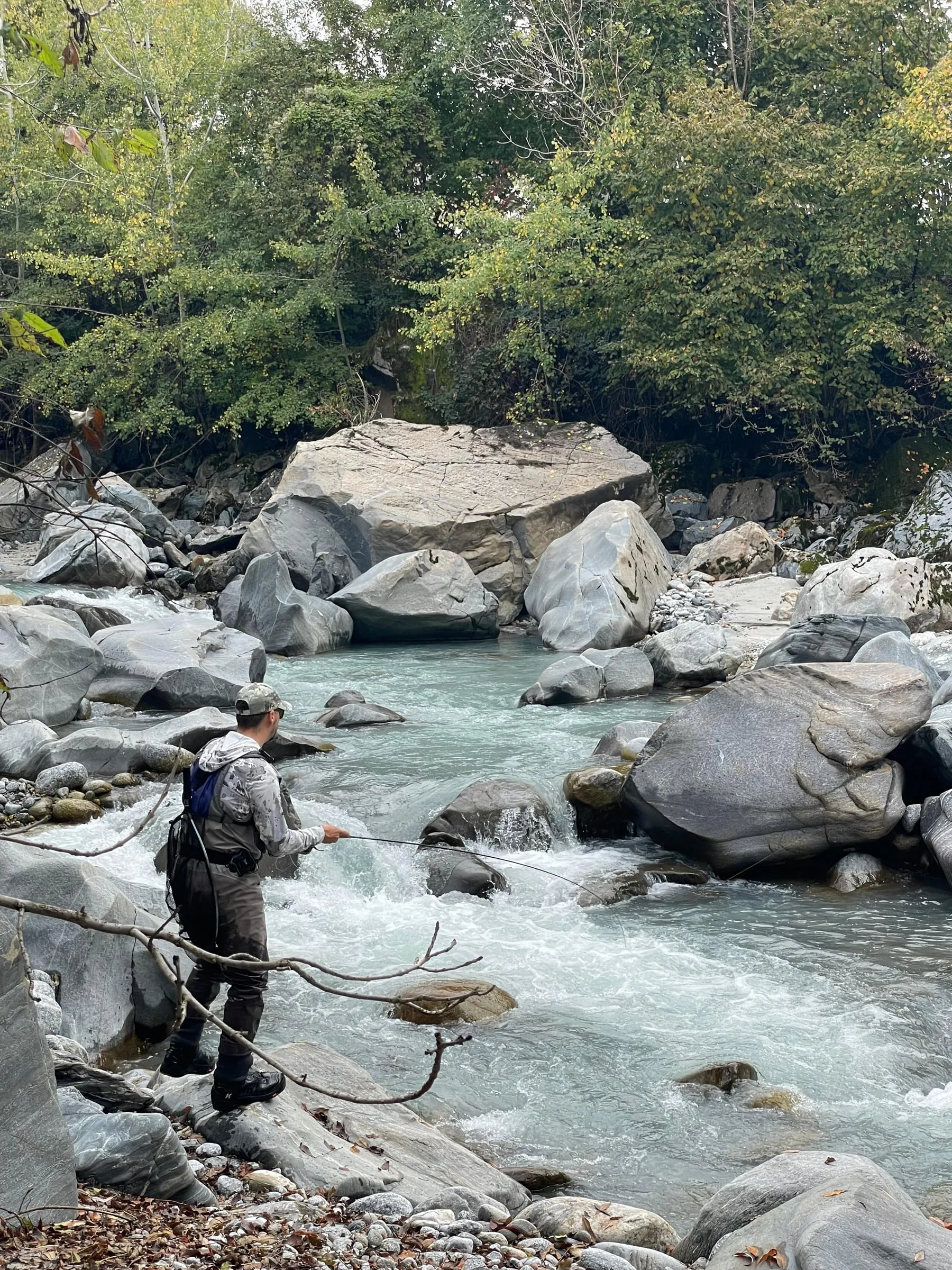 Aleksandar Gasevic casting while wading a boulder-strewn river, another angler further upstream.