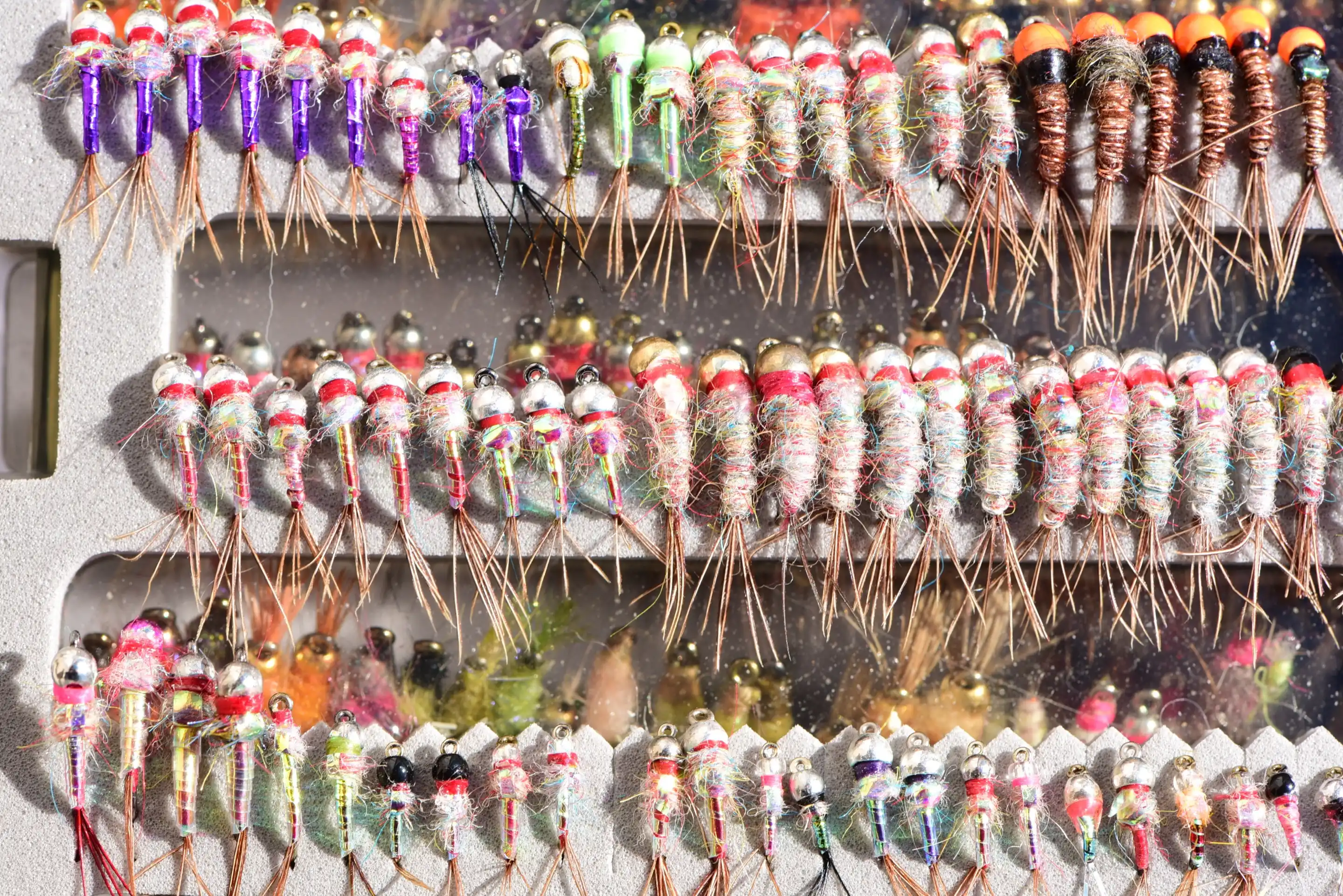 An open fly box packed with rows of bead-head nymphs in pink, purple, orange and green.