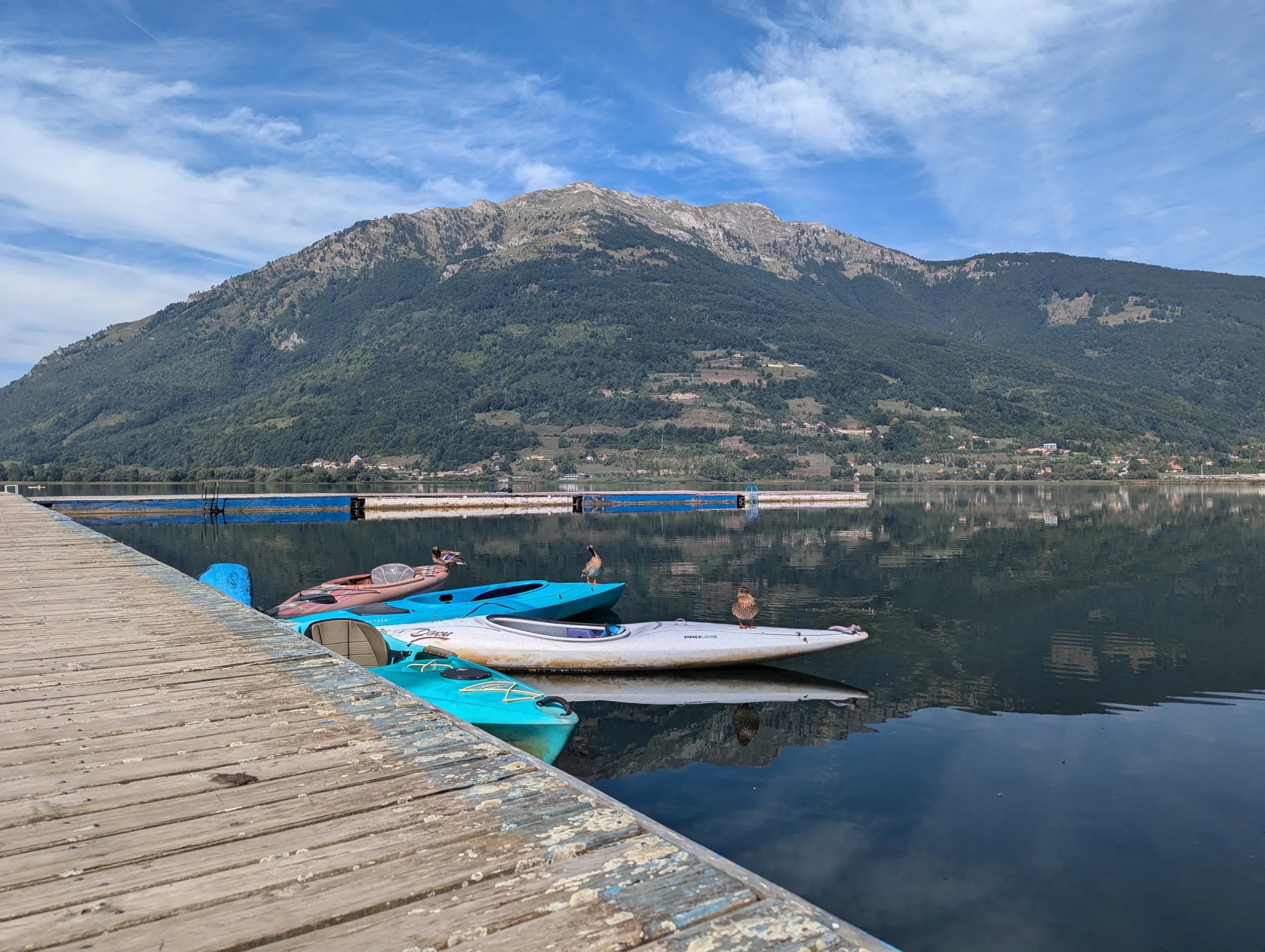 A wooden jetty with small boats on Plav Lake, with a bare mountain behind.