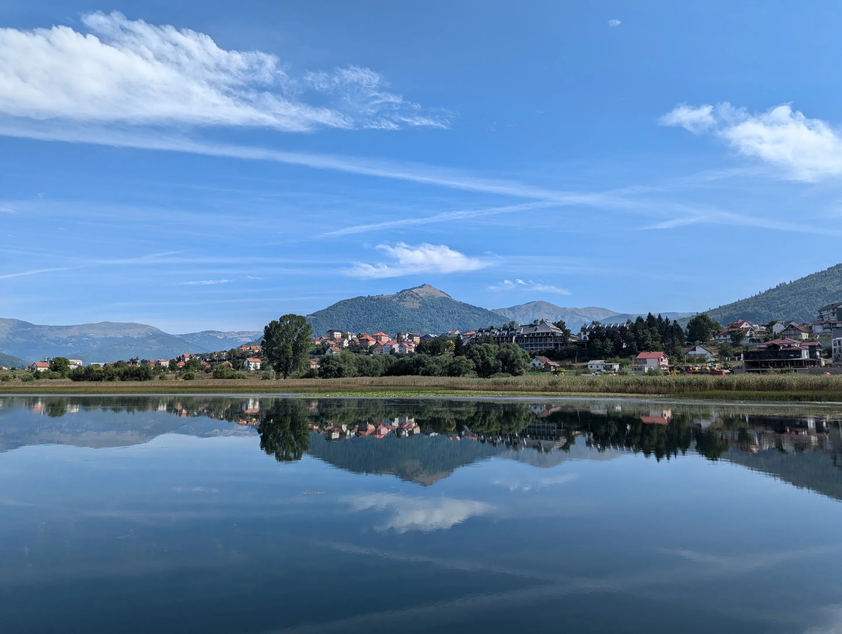 Plav Lake on a still morning, with the town of Plav and the mountains mirrored in the water.