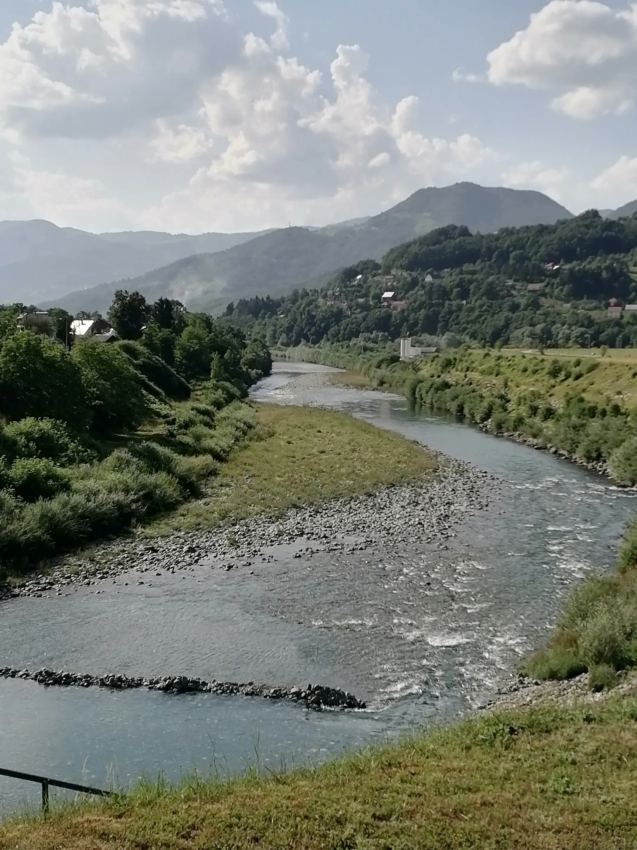 The Tara river at Mojkovac seen from the bank: a gravel bar and a riffle, with wooded hills and a few houses behind.